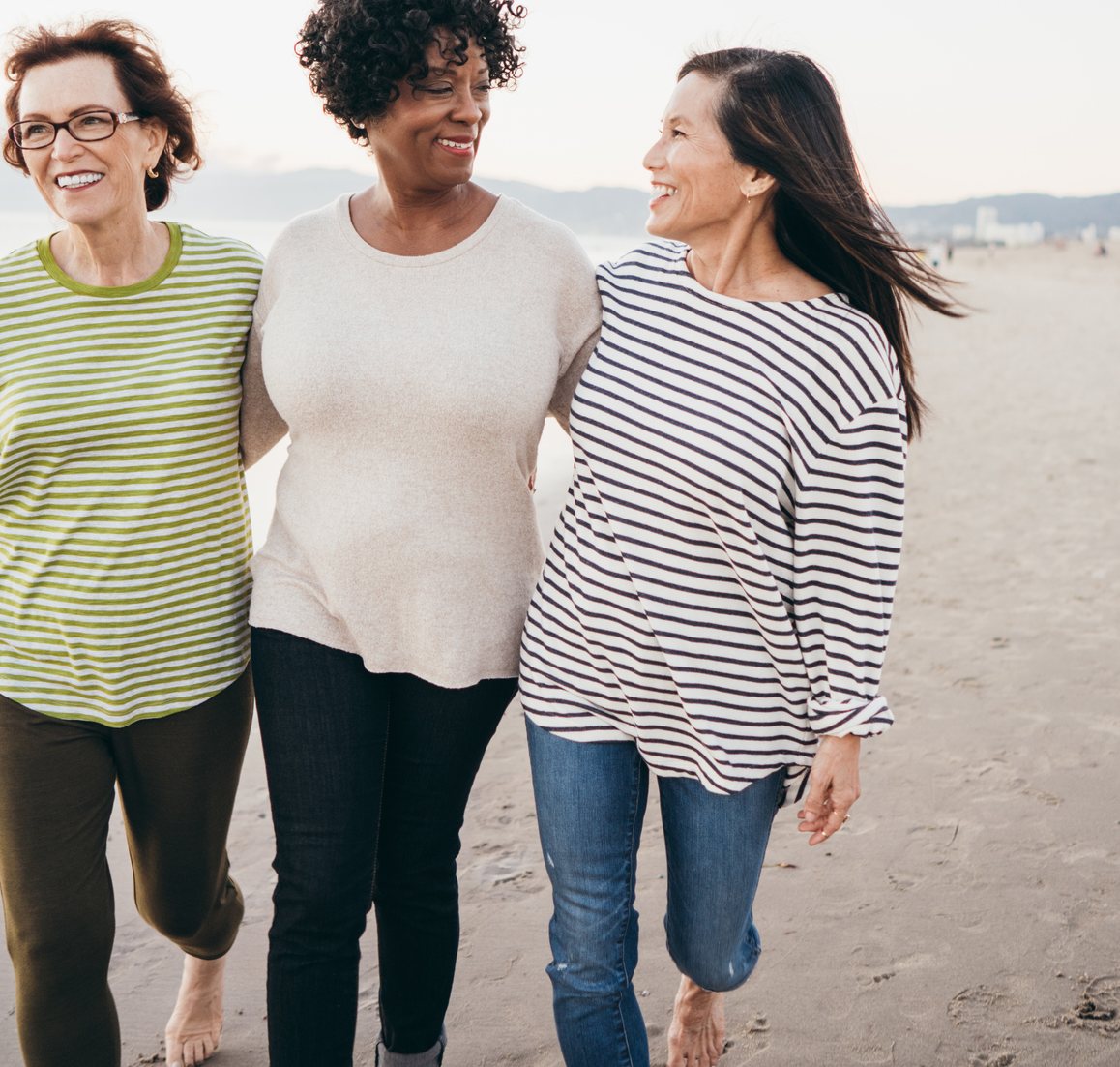 Three women smiling and walking together along the beach